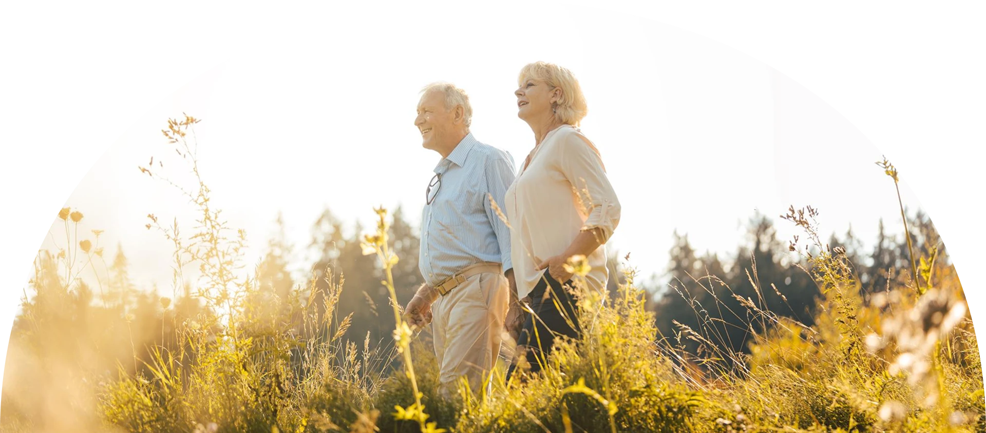 An elderly couple stands in a field.
