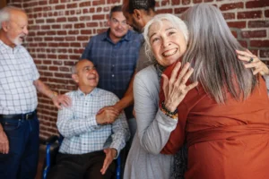 Happy senior woman hugging a friend in a group of older adults, sharing joy and connection in a community setting.