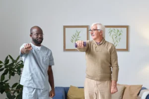 Senior man practicing stroke recovery exercises with light dumbbell alongside physiotherapist.